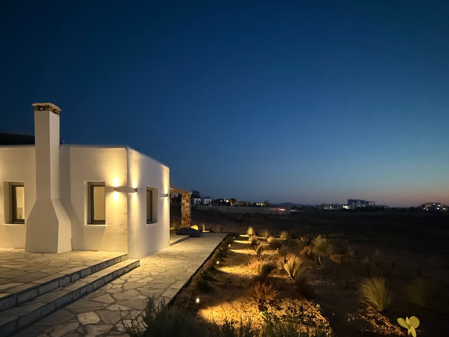 The lit stone paths and native garden beds at DEON under a deep blue night sky