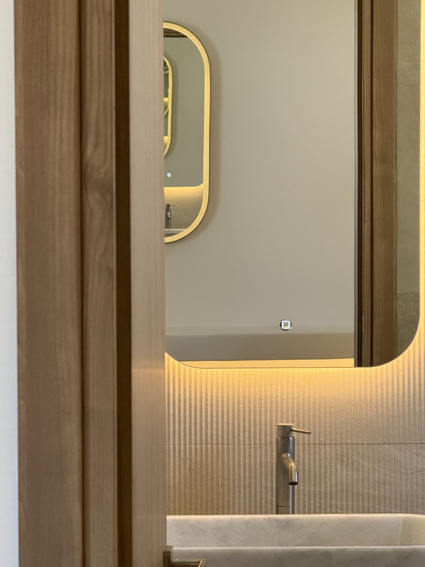 A detail of the washbasin and lit mirror at DEON, seen through a timber doorway