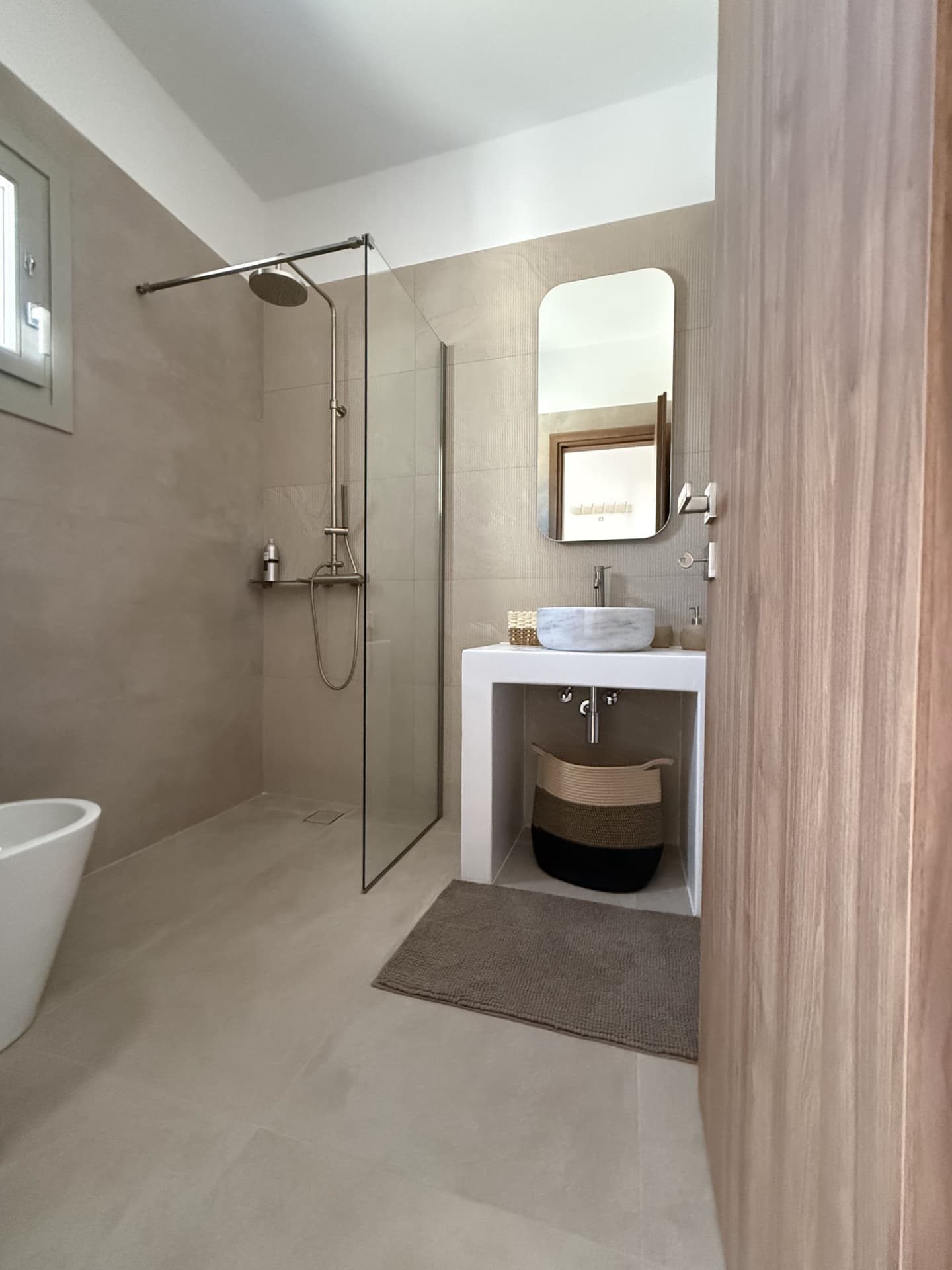 A bathroom at DEON in soft plaster tones with a walk-in shower and marble basin