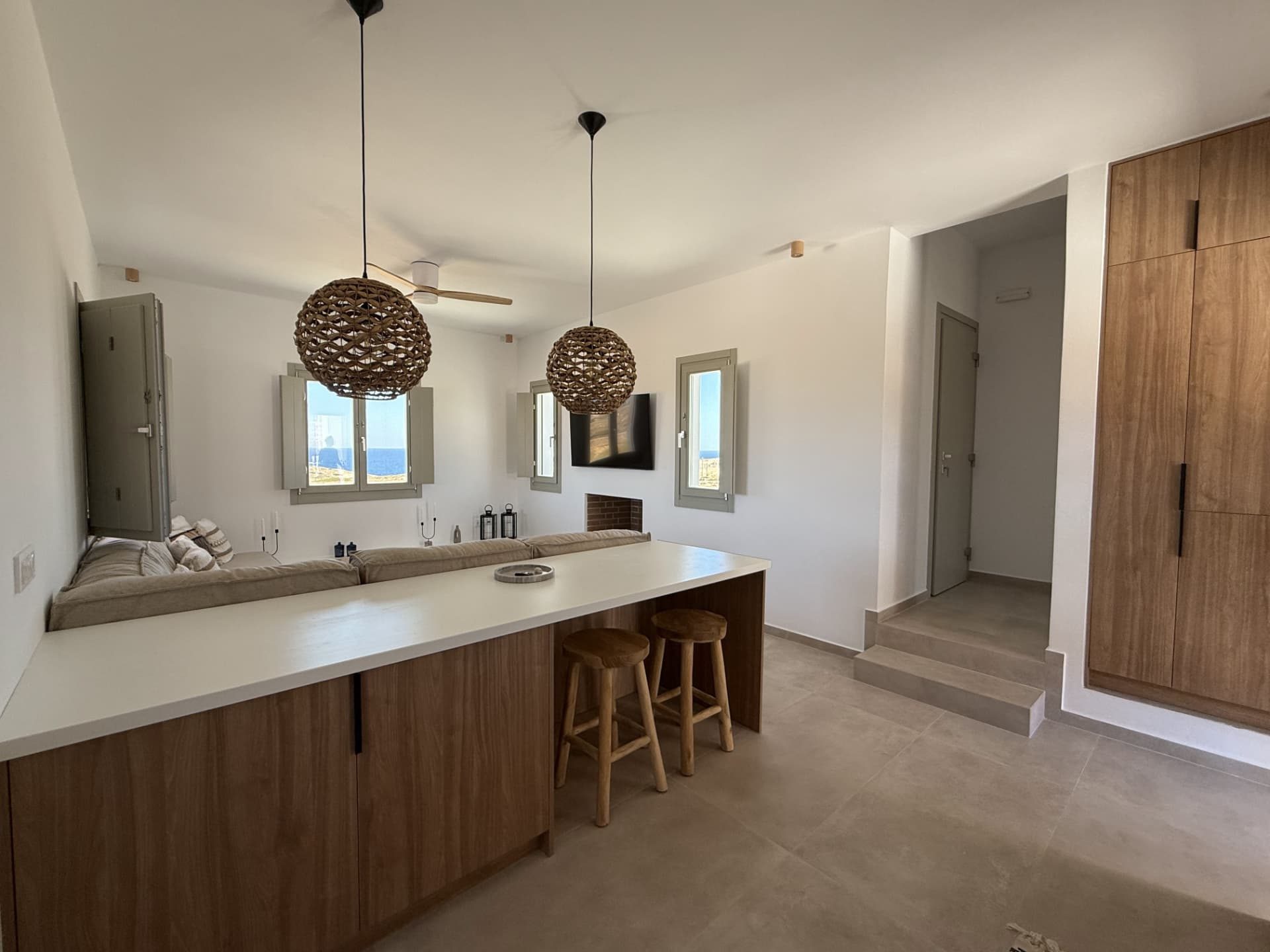 The open kitchen and living room at DEON, with woven pendants and sea views through shuttered windows