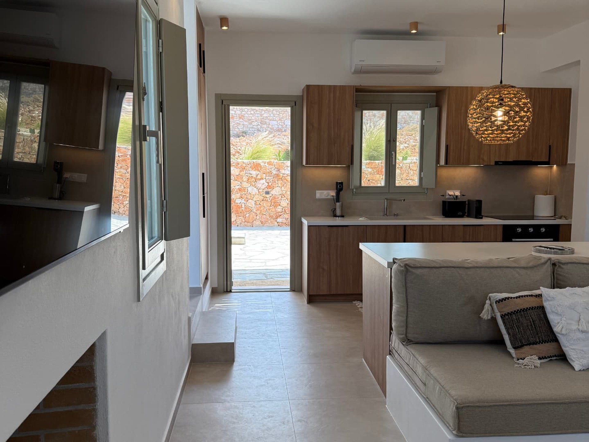 The open kitchen and living room at DEON, with the sea visible through the open door to the stone terrace