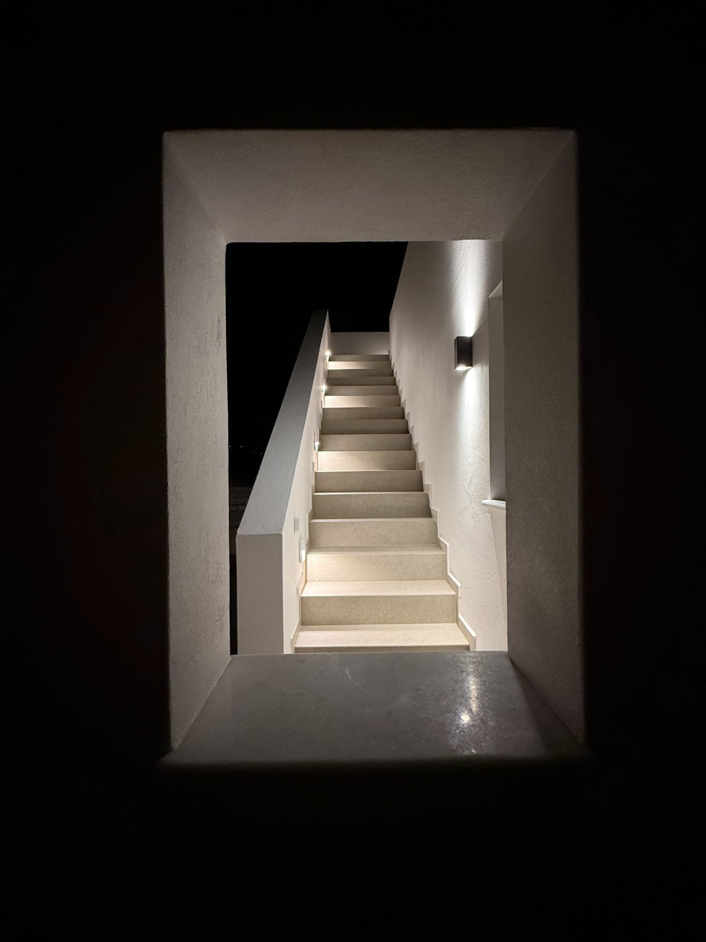 The lit exterior stair at DEON at night, framed through a deep plaster window opening