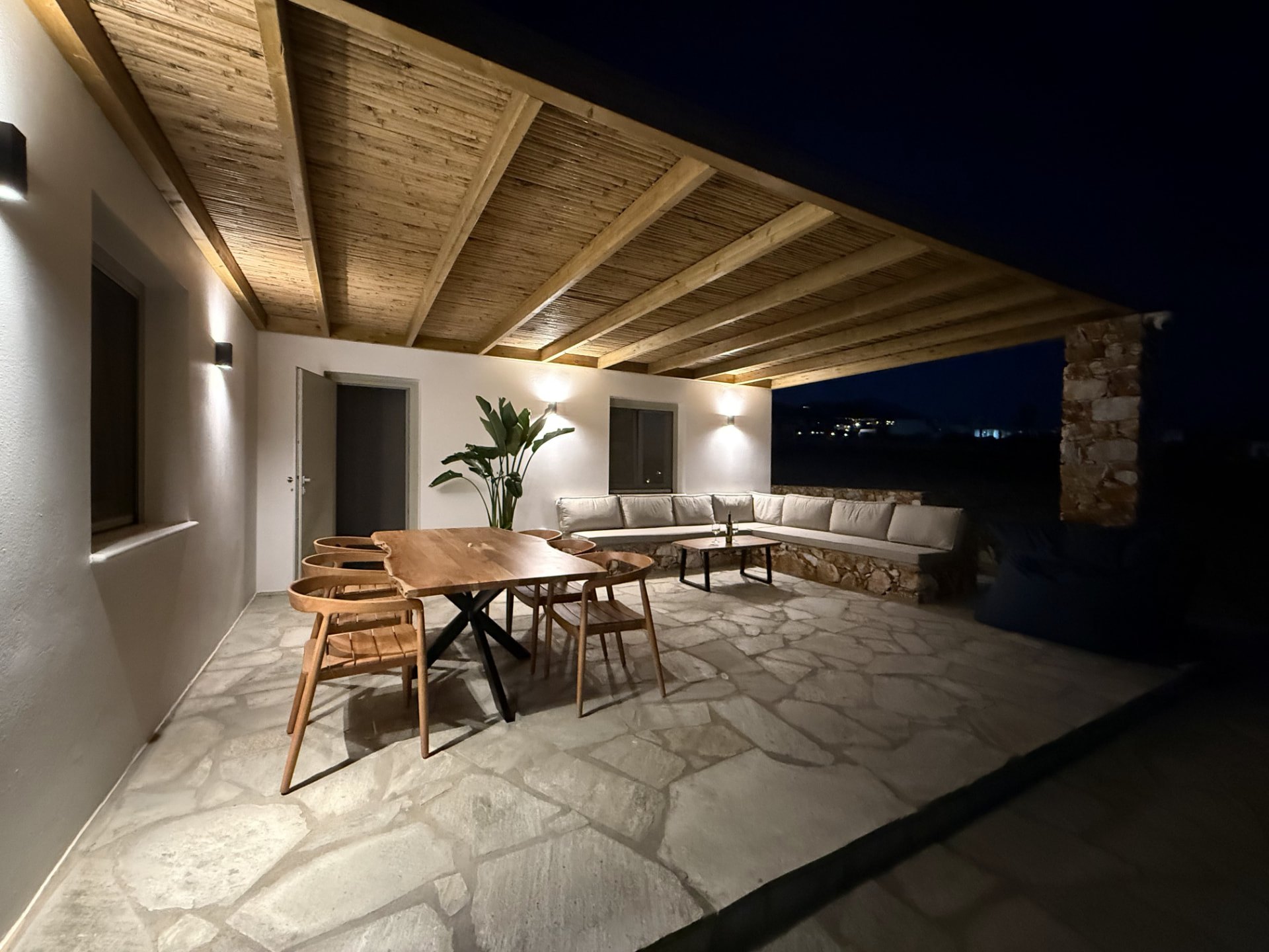 The covered terrace at DEON at night, timber pergola above a dining table and long stone-built sofa