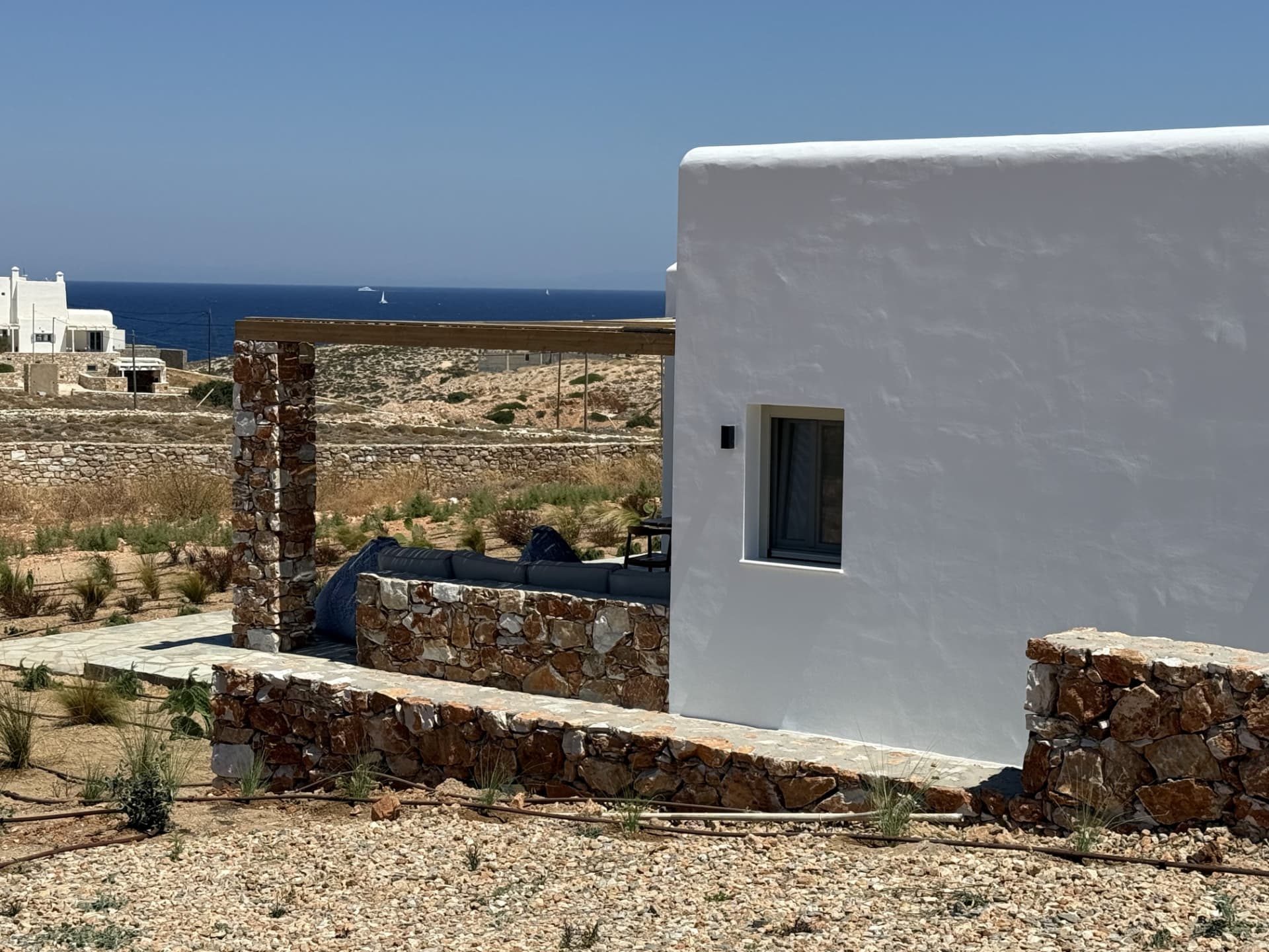 The whitewashed west facade of DEON with its stone terrace and the Aegean beyond